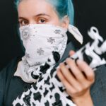 A person with blue hair and a bandana holding a black and white rifle, conveying protest themes.
