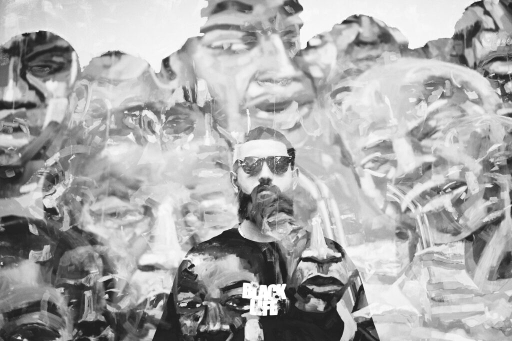 Man with sunglasses in front of vibrant urban mural art, black and white.