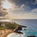 Stunning aerial shot of the Rincón lighthouse overlooking a tropical beach and the Atlantic Ocean in Puerto Rico.
