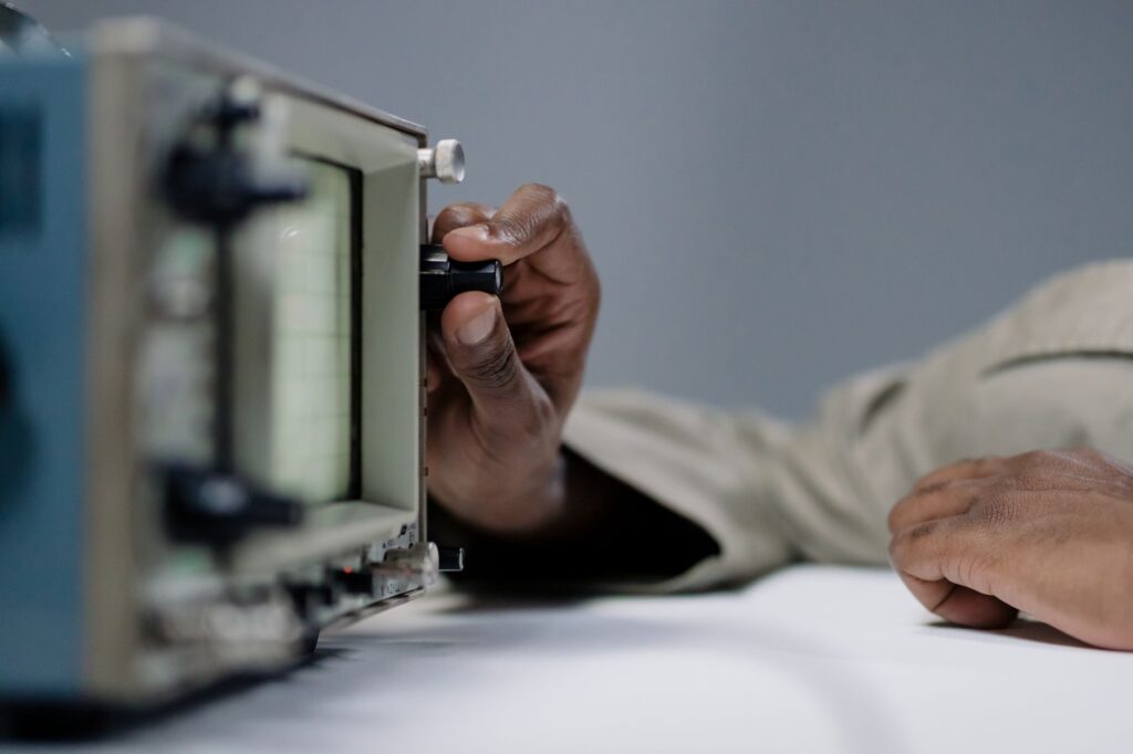 Detailed view of a person's hand adjusting a knob on an oscilloscope in a studio setting.
