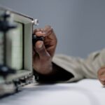 Detailed view of a person's hand adjusting a knob on an oscilloscope in a studio setting.