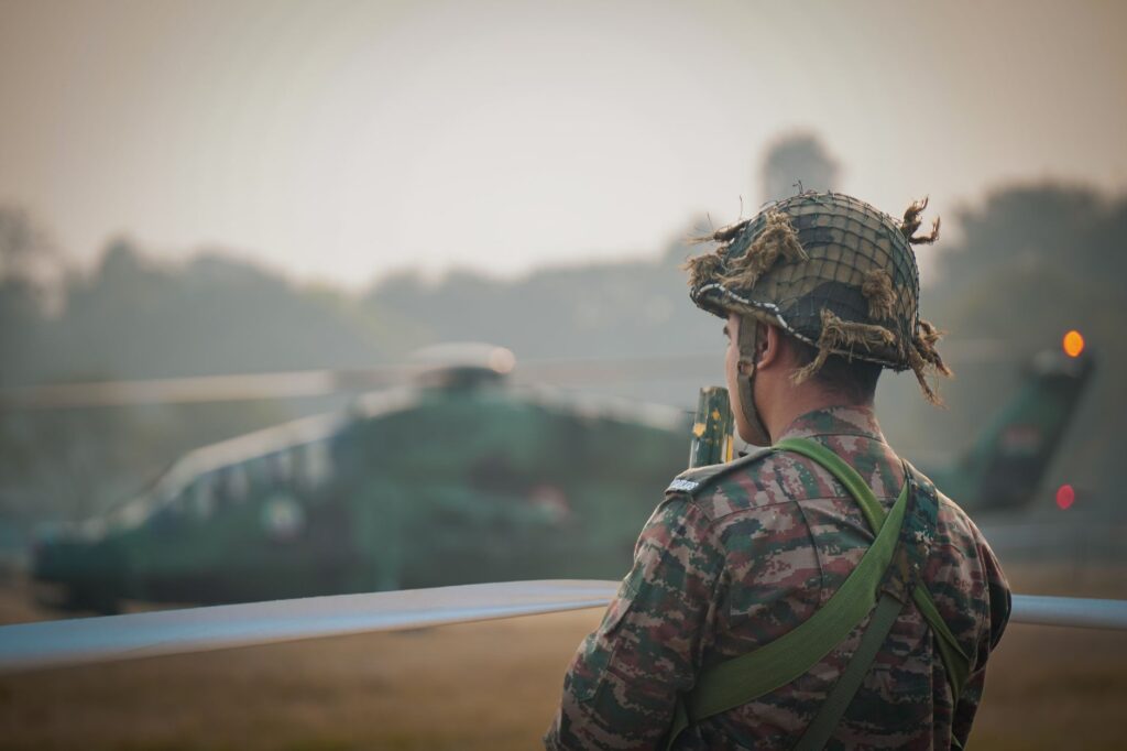 A soldier in camouflage stands with a helicopter in the background, Kolkata, India.