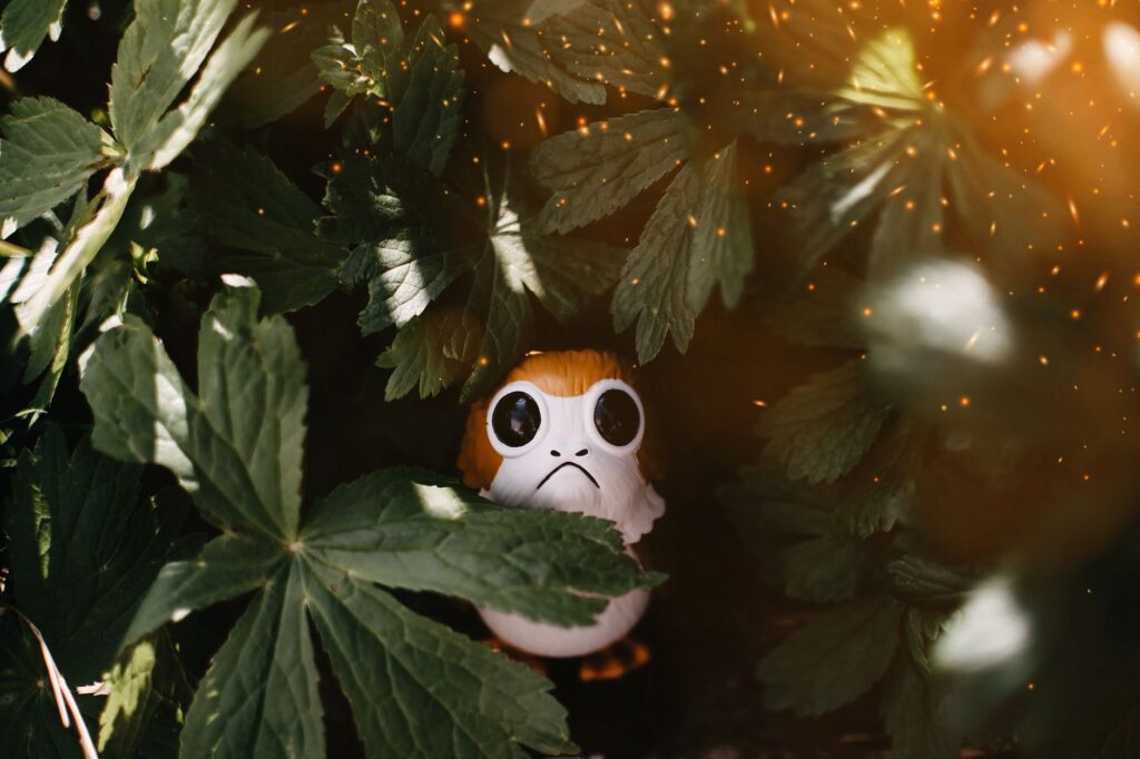 A captivating close-up of a toy Porg hidden among lush green leaves with sparkling light effects.