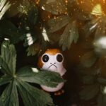 A captivating close-up of a toy Porg hidden among lush green leaves with sparkling light effects.