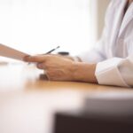 Close-up of a doctor in a lab coat reviewing paperwork at a desk.