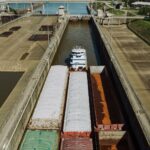 From above of old industrial transport carrying heavy containers with rusty surface on water channel near green meadow in harbor