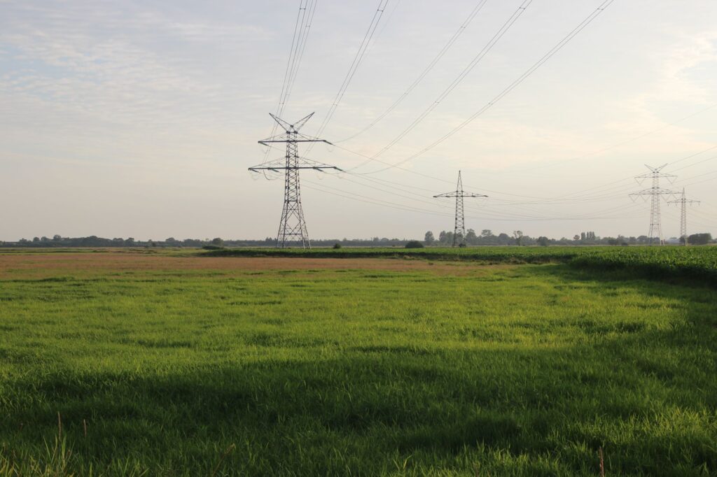 Wide green field with power lines under a cloudy sky in Northern Germany.