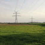 Wide green field with power lines under a cloudy sky in Northern Germany.