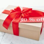 Cardboard gift box with a vibrant red ribbon offering a 50% off discount.