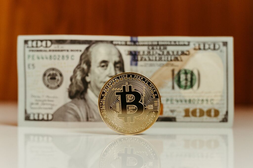 Close-up of a Bitcoin digital currency with a US hundred-dollar bill in the background.