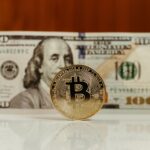 Close-up of a Bitcoin digital currency with a US hundred-dollar bill in the background.
