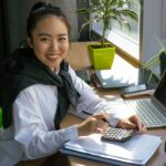 Confident woman working with calculator in bright office setting, surrounded by office tools.