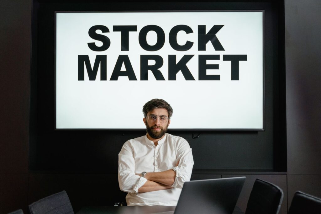 Confident businessman sitting in front of a stock market display screen in a modern office setting.