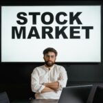 Confident businessman sitting in front of a stock market display screen in a modern office setting.