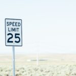 White sign on roadside with speed limit against empty green field at daytime
