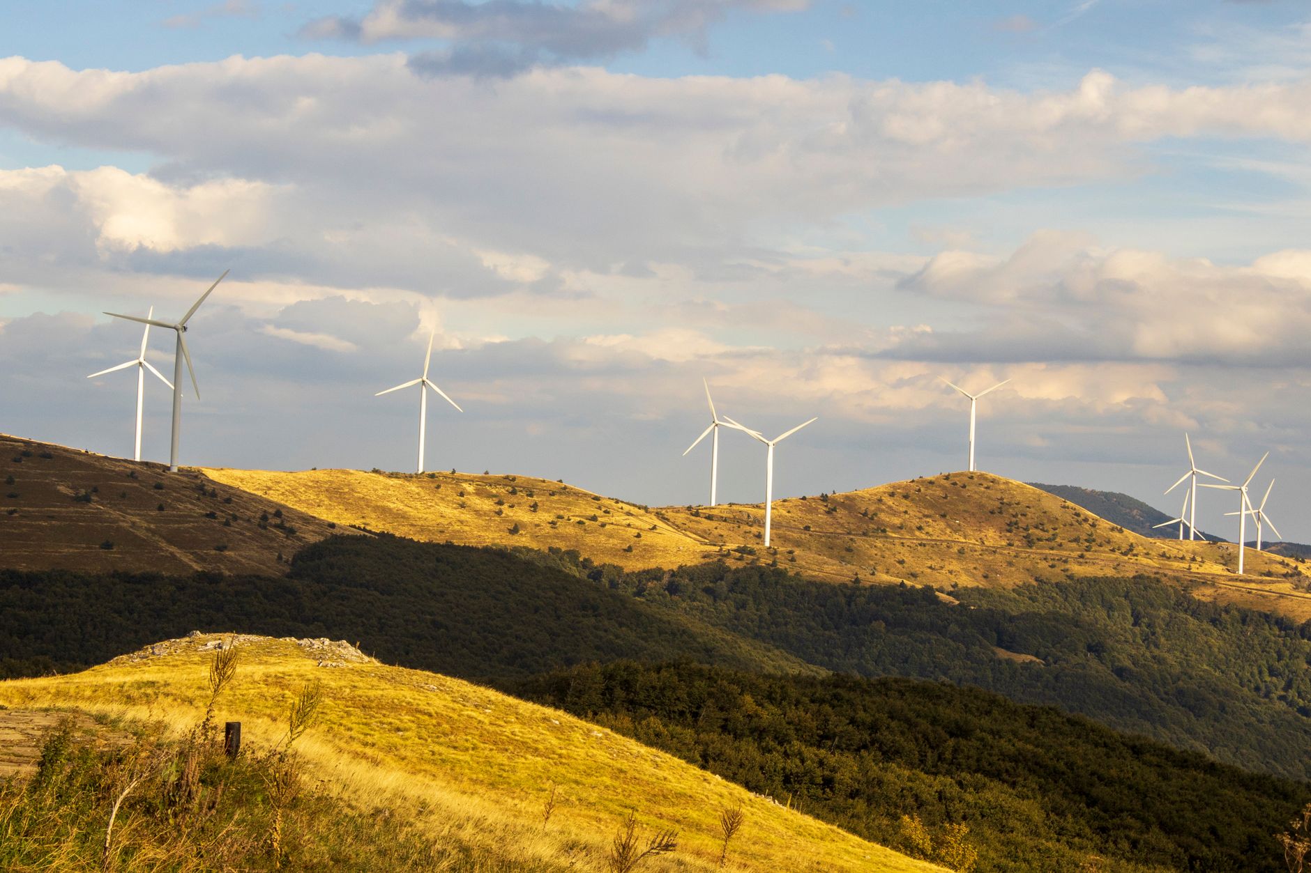 Wind turbines on green hills showcase renewable energy amidst a scenic landscape under a cloudy sky.