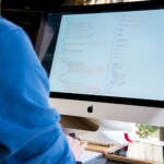 A programmer in a blue shirt coding on an iMac. Perfect for technology or work-related themes.