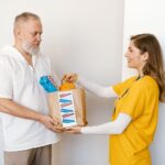 Elderly man receives donation package from smiling volunteer indoors.