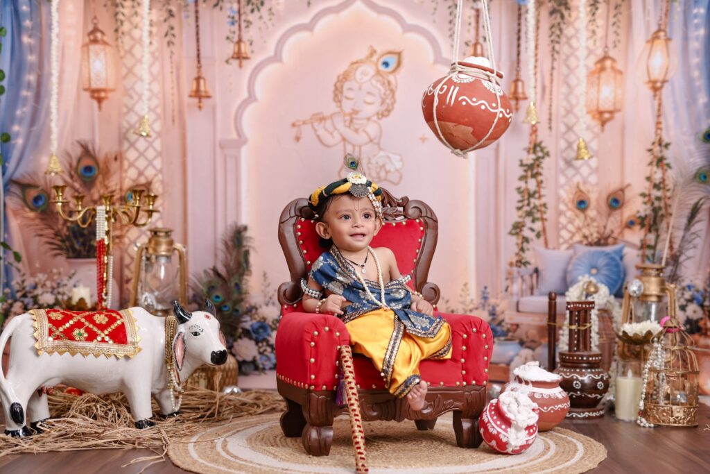 Adorable baby dressed as Lord Krishna surrounded by traditional festive decor and colorful pottery.