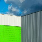 Close-up of a modern building facade with colorful panels and corrugated metal against a dramatic blue sky.