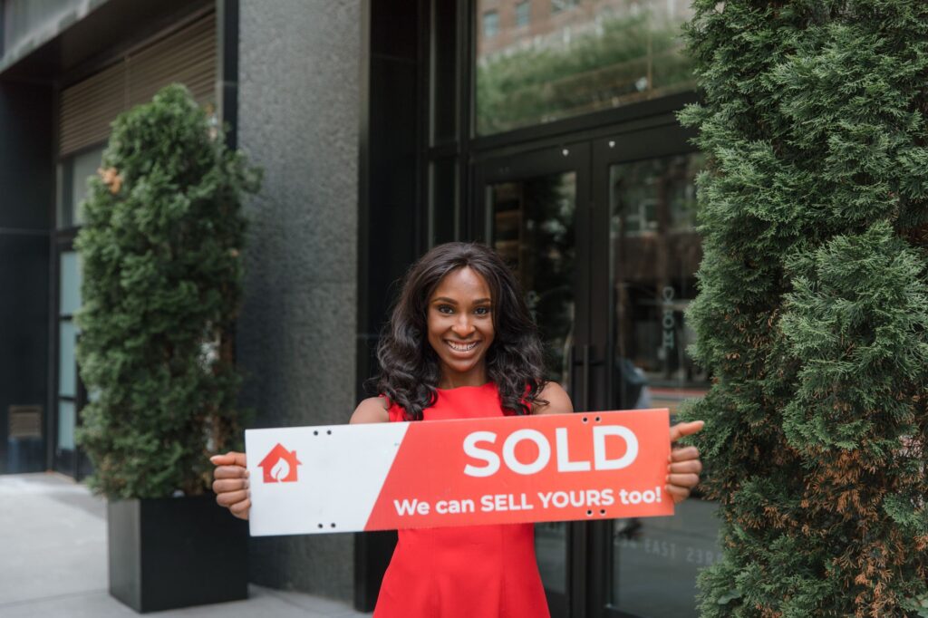 Confident real estate agent holds 'SOLD' sign in front of building, symbolizing success.
