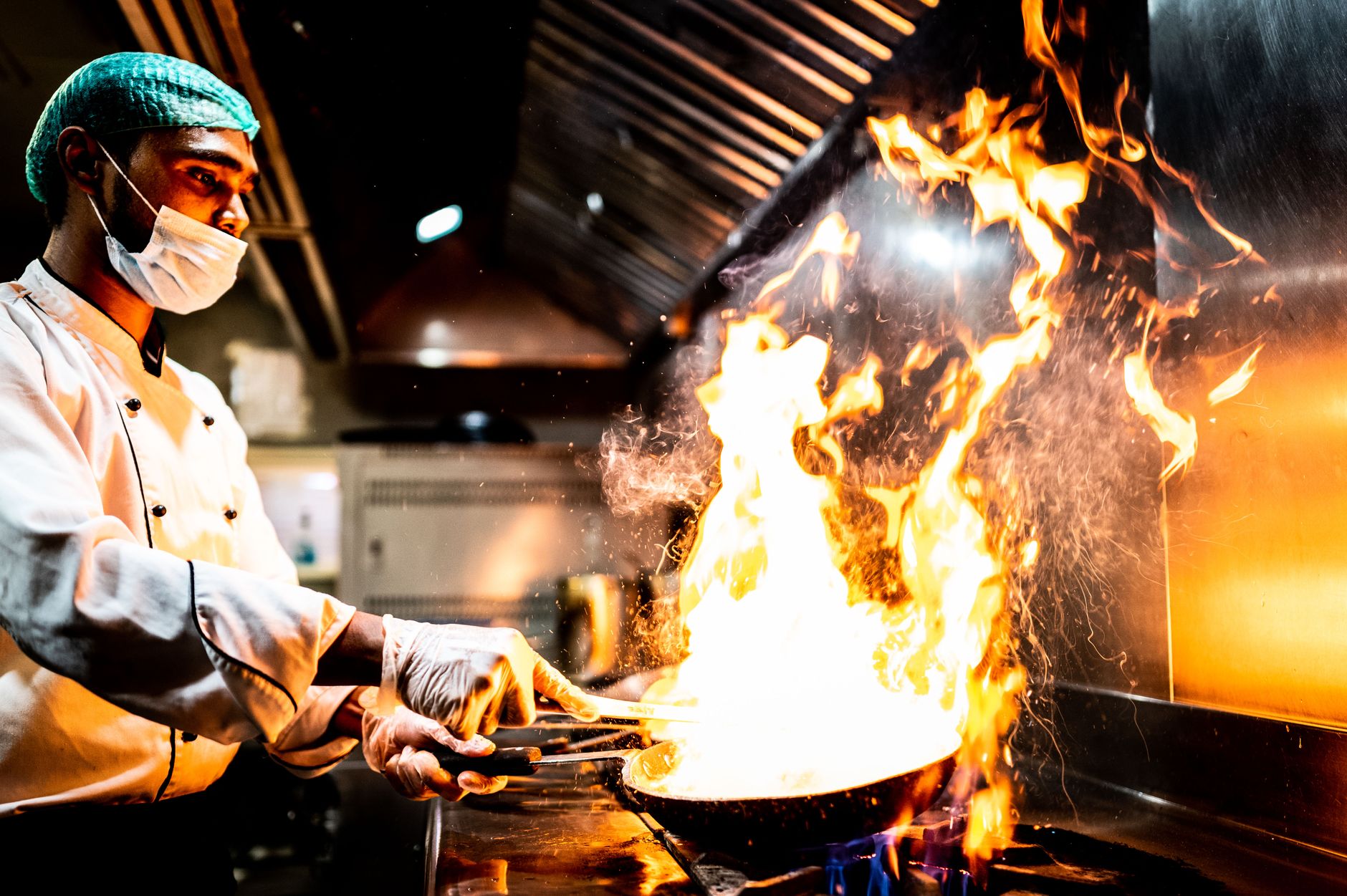 A skilled chef performs a dramatic flambé cooking technique in a professional kitchen setting.