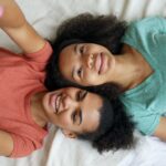 Two teenage girls lying on a bed, smiling while taking a selfie, capturing a joyful moment.