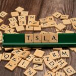 Wooden letter tiles spell TSLA, hinting at the stock market and investment themes.