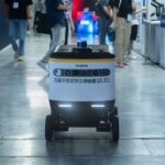 Autonomous delivery robot navigating indoors during a technology event.