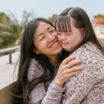 Loving mother embraces her daughter with Down syndrome, showcasing affection and happiness.