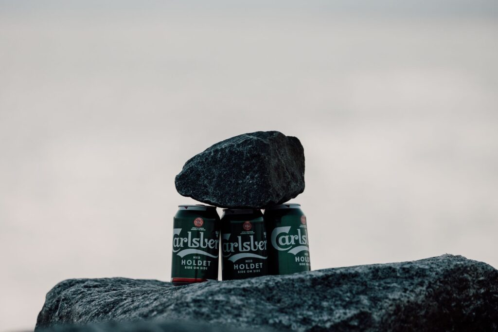 Three Carlsberg beer cans supported by rocks with an ocean backdrop, creating a unique still life.