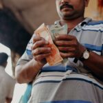 Man in Indian market counting rupee notes, showcasing daily street commerce.