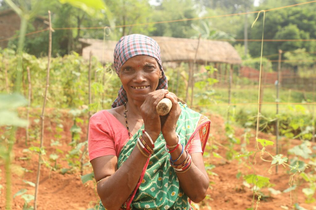 Elderly woman farmer smiling in a vibrant countryside garden with green crops.
