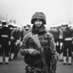 A soldier stands in focus during a military parade in monochrome.