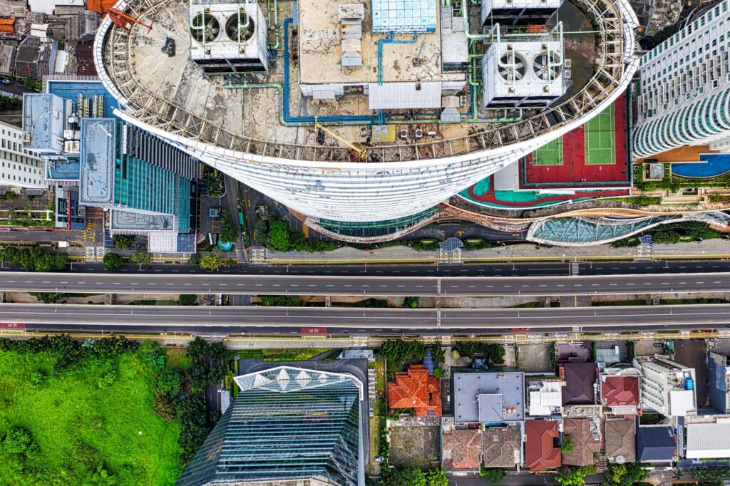 Drone shot capturing Jakarta's urban skyline with high-rise buildings, roads, and green areas.
