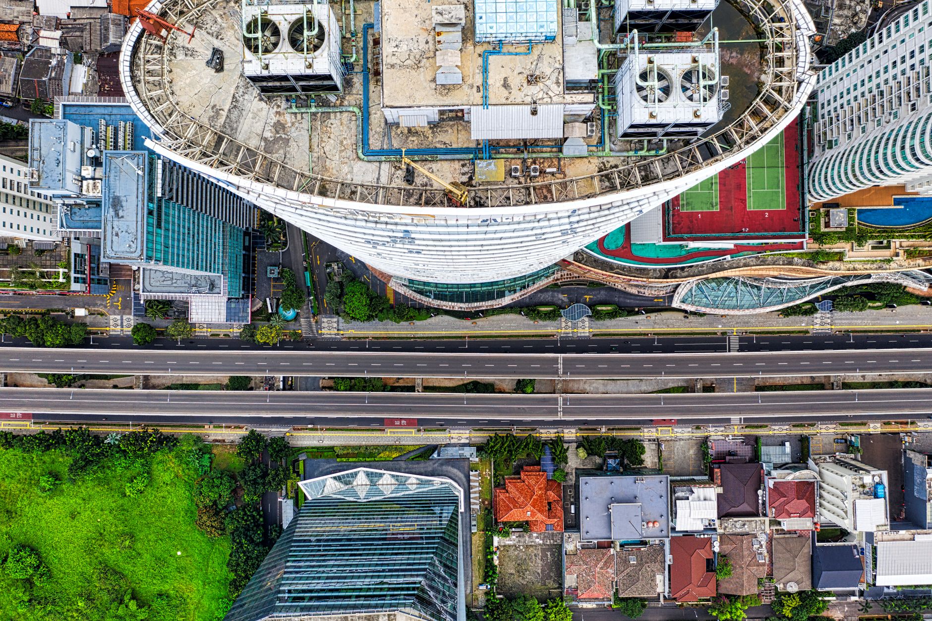 Drone shot capturing Jakarta's urban skyline with high-rise buildings, roads, and green areas.