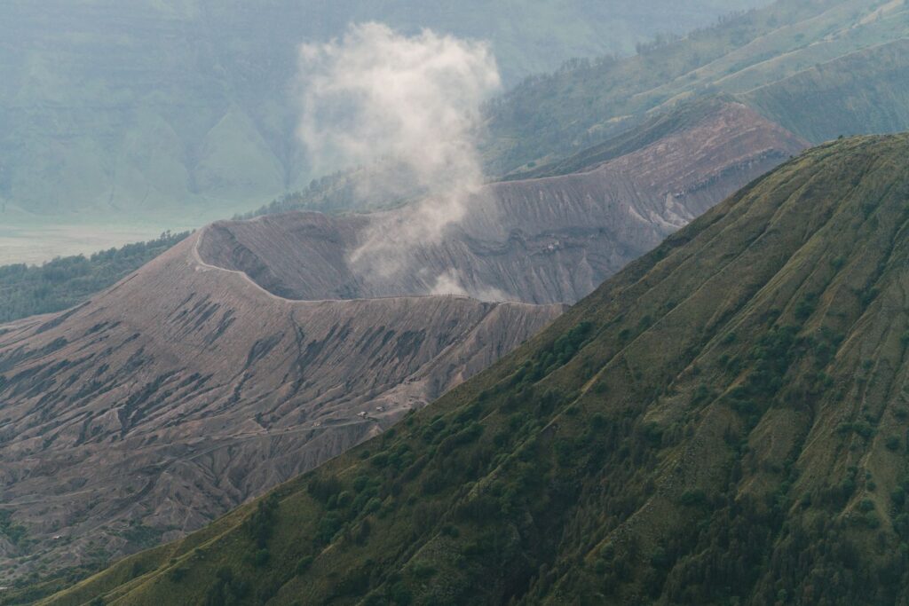 A dramatic view of a volcano crater emitting smoke amidst verdant mountains.