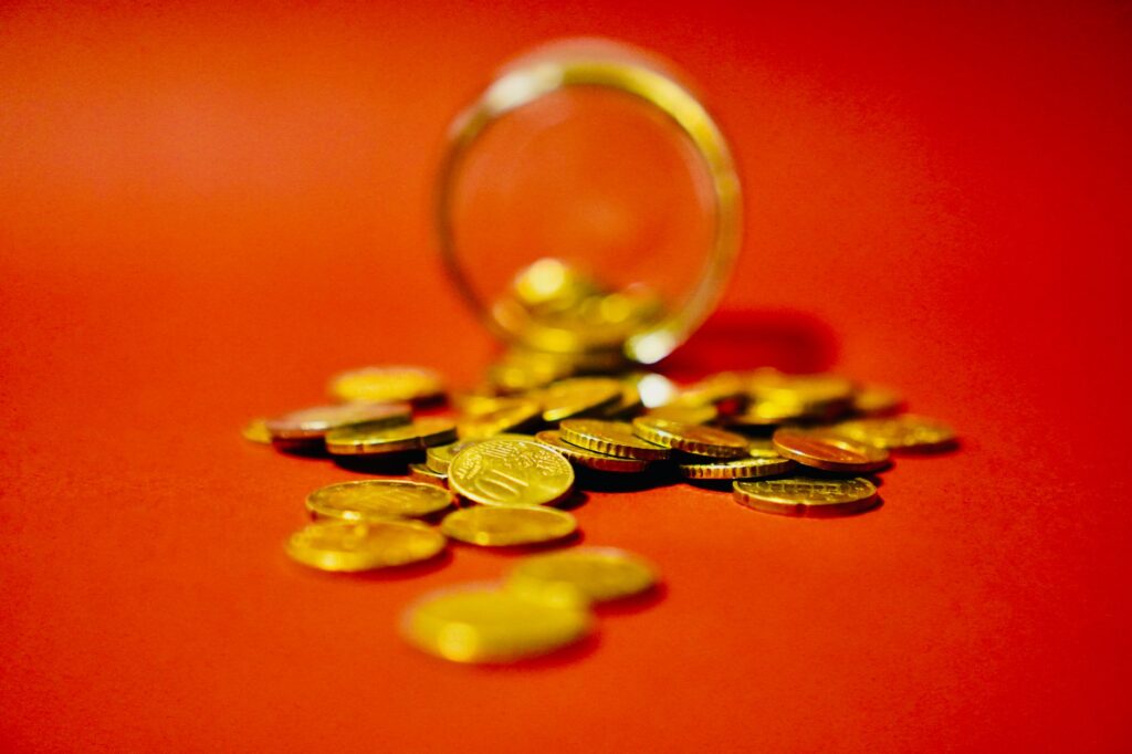 A collection of golden coins spilling from a glass jar on a vibrant red background symbolizes wealth.