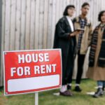Three adults examining a house for rent sign outdoors, depicting diverse and inclusive interest in rental properties.