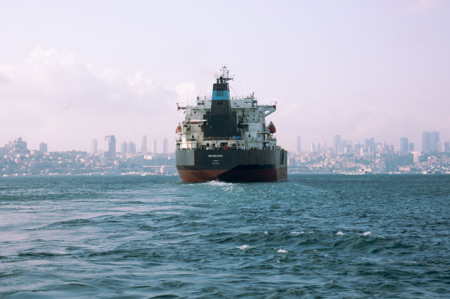 Large cargo ship sails through Istanbul's Bosphorus with city skyline in background.