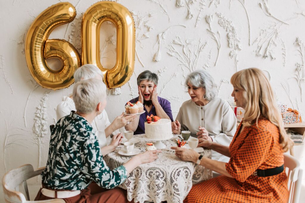 Senior women joyfully celebrating a 60th birthday with cake and decorations.
