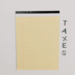 Close-up of a yellow legal pad and the word 'TAXES' on a white surface, ideal for finance themes.