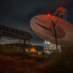 A nighttime view of a satellite dish at Madrid Deep Space Communications Complex under a dark sky.