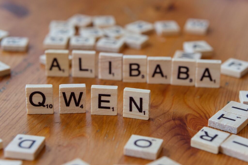 Close-up of Scrabble tiles spelling 'Alibaba' and 'Qwen' on a wooden surface.