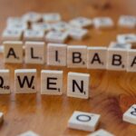 Close-up of Scrabble tiles spelling 'Alibaba' and 'Qwen' on a wooden surface.