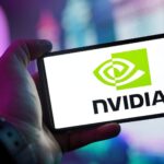 Close-up of a hand holding a smartphone showing the NVIDIA logo on screen with a blurred background.