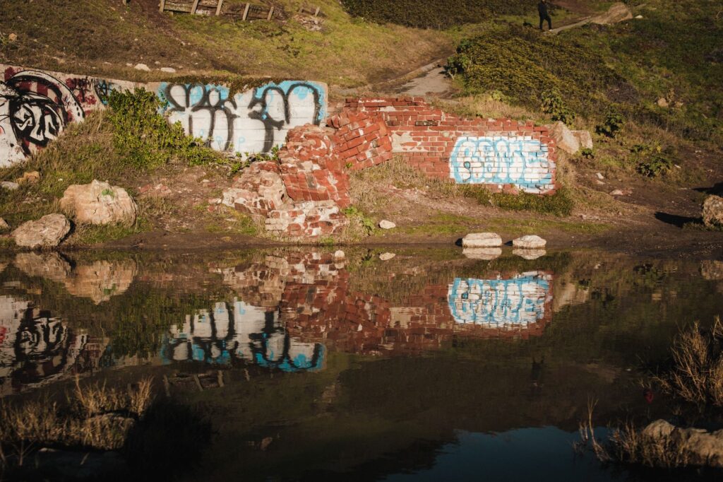 A serene outdoor scene of graffiti-covered brick wall reflecting in a calm pond.