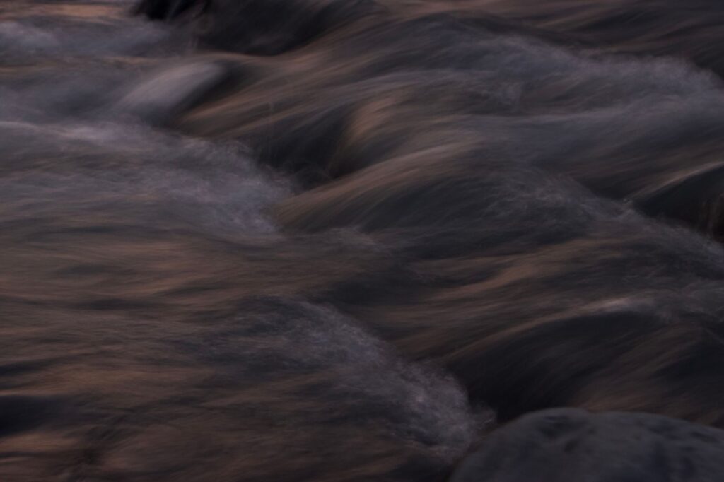 Close-up of a dark and wavy water stream captured at twilight, conveying serenity.