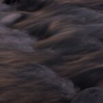 Close-up of a dark and wavy water stream captured at twilight, conveying serenity.