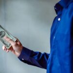 A person in a blue shirt holding a stack of US dollar bills, symbolizing wealth and finance.